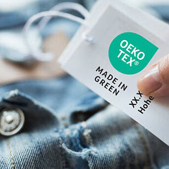 Chaqueta en mezclilla con mano sujetando una etiqueta OEKO-TEX® MADE IN GREEN