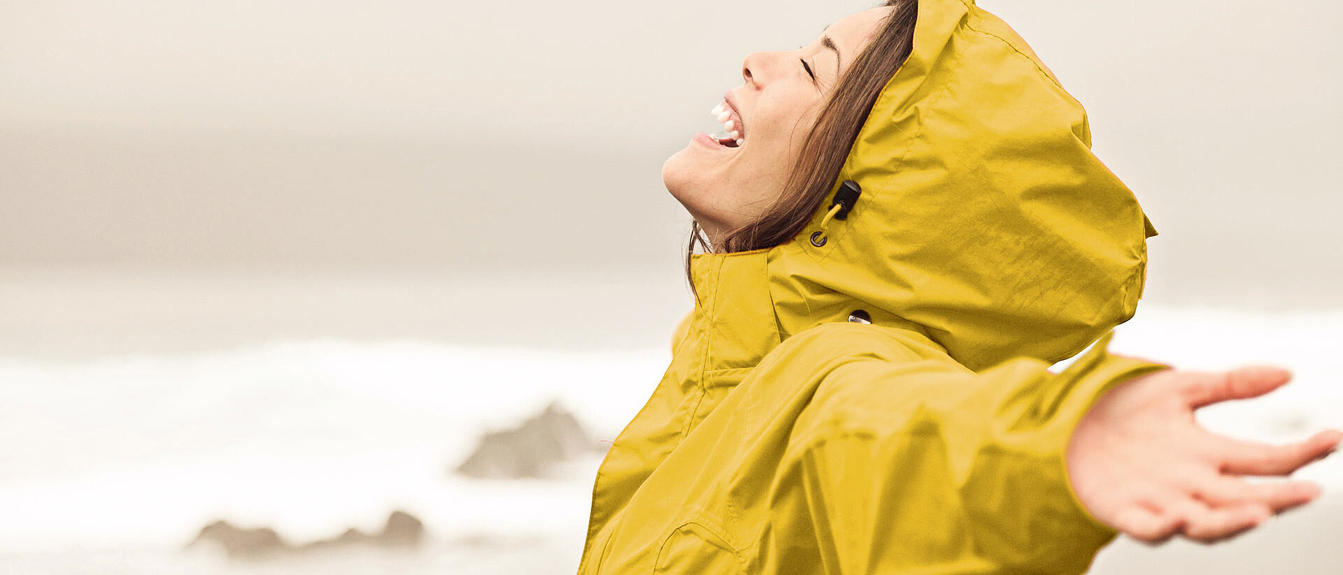 Mujer con impermeable amarillo con los brazos extendidos