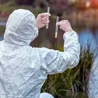 Auditor tomando muestras de aguas residuales de un arroyo cerca de una planta textil