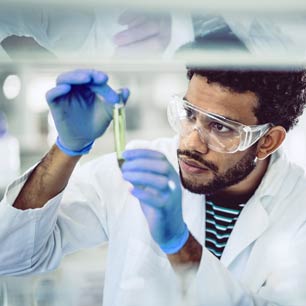 Hombre vestido con guantes azules y bata de laboratorio con vial de productos químicos textiles