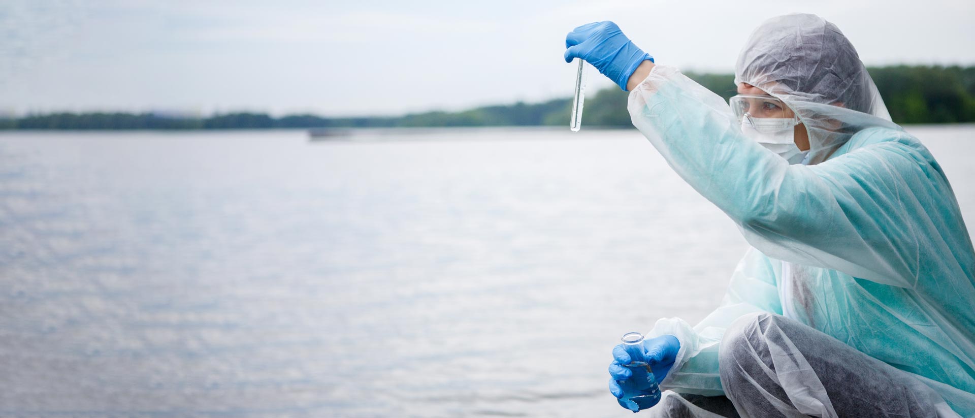 Técnico de laboratorio con equipo en protección tomando muestras de aguas residuales en un río.