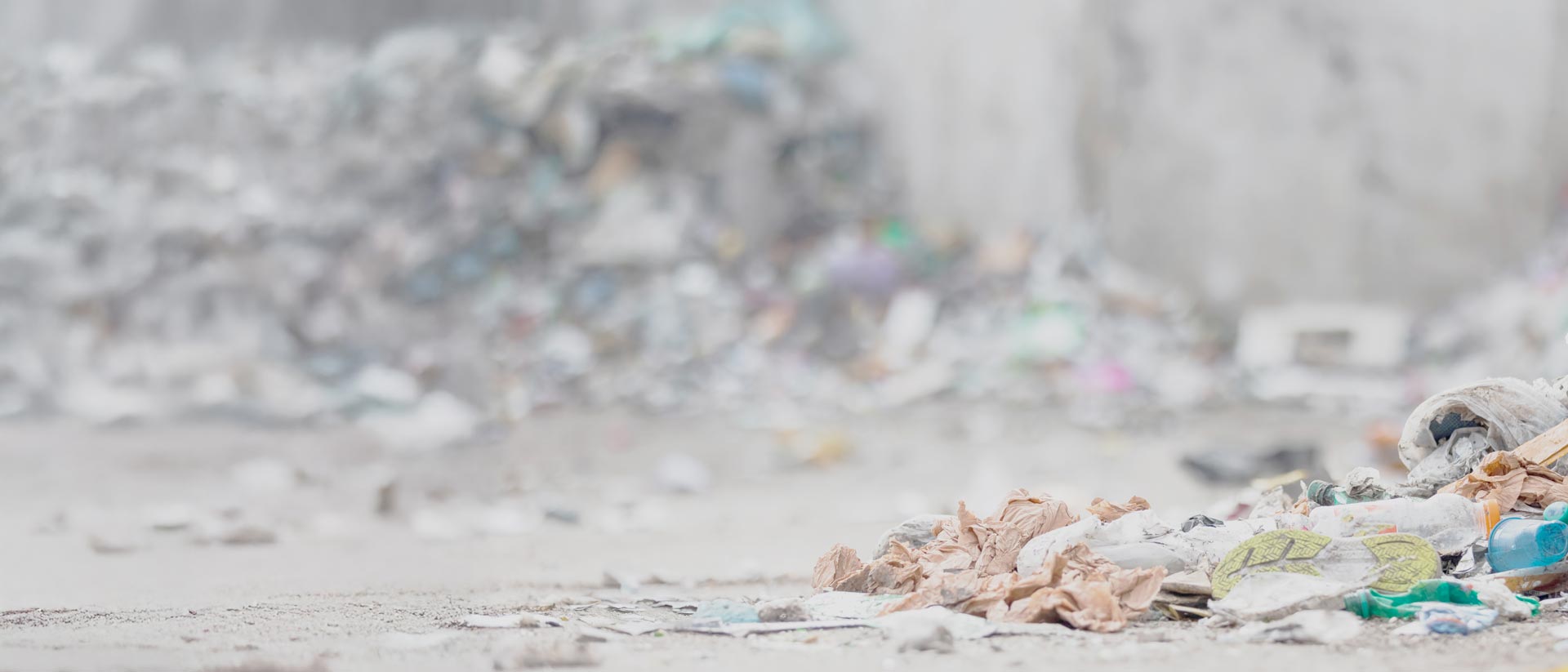 Zapato, ropa y botellas de plástico desechados cerca de un gran montón de basura.