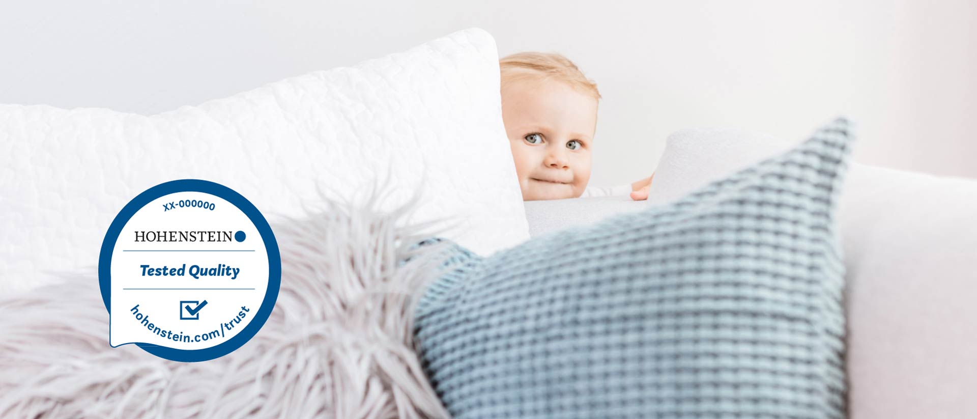 Niño detrás de un sofá con almohadas y un Sello de Calidad Hohenstein