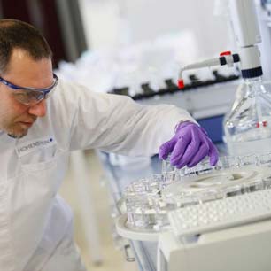 Trabajador de laboratorio con guantes morados y bata de laboratorio, examinando viales de productos químicos textiles en el laboratorio