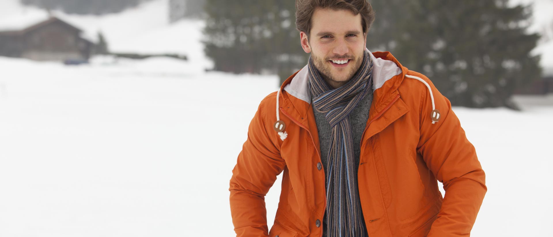 hombre de pie en la nieve, vestido con una chaqueta aislante naranja y una bufanda negra