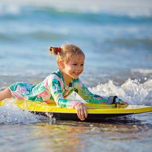 Chica en traje de baño con protección UV en tabla de surf en la playa