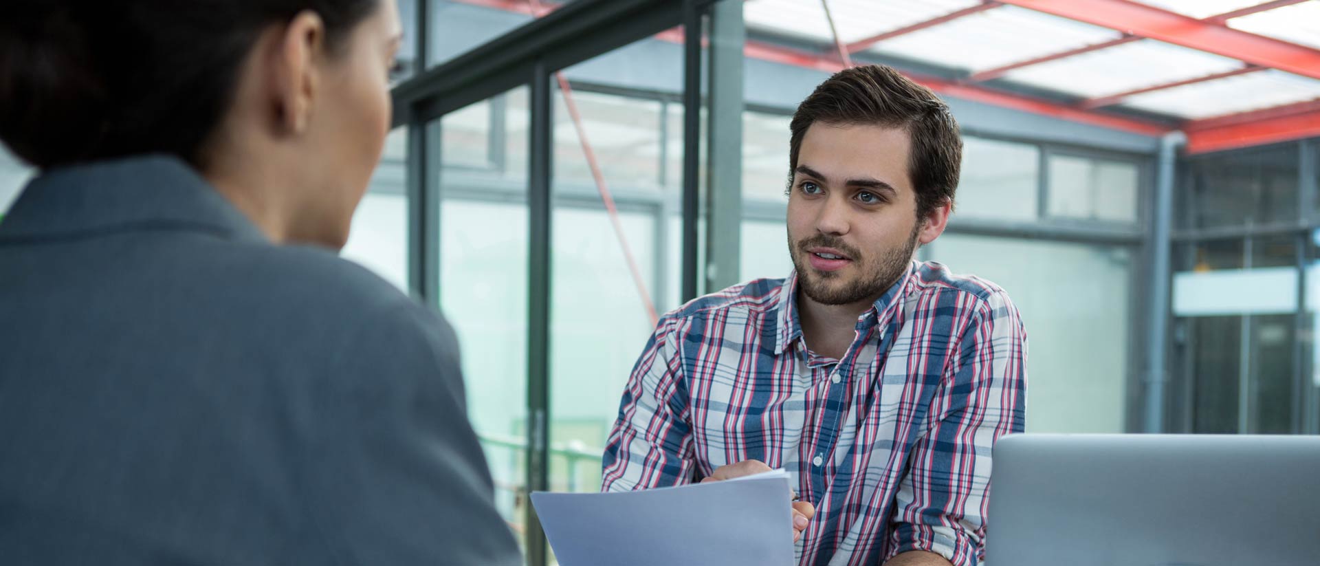 Dos personas hablando en una mesa con una laptop y papel